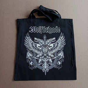 Pode incluir: Sacola de lona preta com um design gráfico branco de uma criatura alada com duas cabeças e o texto "Wolffbrigade".