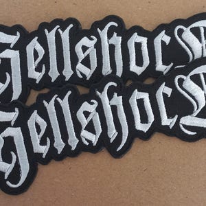 May include: Two black fabric patches with white embroidered text that reads "Hell's Bells" in a gothic font.