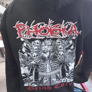 May include: Black hooded sweatshirt with a white and red graphic print of a skull wearing a gas mask and the words "PHOENIX Grind Core".