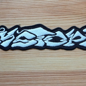 May include: White embroidered patch with the word "SODOM" written in a stylized, graffiti-like font.