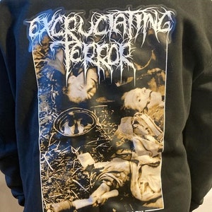 May include: Black hooded sweatshirt with a white graphic print of a band logo "Excruciating Terror" and a black and white image of a person lying on the ground with the text "Expression of Pain".