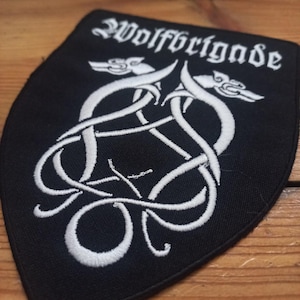 Op de afbeelding: Een zwarte geborduurde patch met witte stiksels die twee in elkaar verweven wolven afbeeldt met de tekst "Wolfbrigade" erboven.