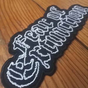 May include: Black embroidered patch with white stitching that reads "Fear of Extinction".