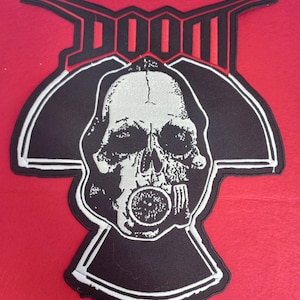 Könnte beinhalten: Schwarz-weiß gestickter Patch mit einem Totenkopf, der eine Gasmaske trägt, und dem Wort "DOOM" in Rot darüber.