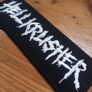 Op de afbeelding: Zwarte geborduurde patch met witte tekst "HELL IS OTHER PEOPLE".
