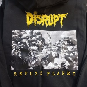 May include: Black hoodie with a yellow graphic print of the word "DISRUPT" and a black and white image of the Statue of Liberty surrounded by debris. The text "REFUSE PLANET" is printed in yellow below the image.