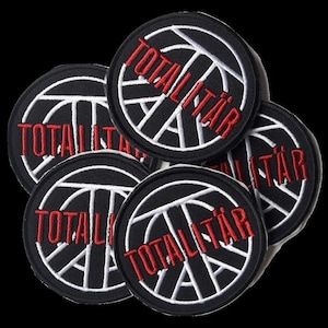 Könnte beinhalten: Sechs schwarze und weiße gestickte Patches mit dem Wort "TOTALITÄR" in roten Buchstaben. Die Patches zeigen ein stilisiertes Basketball-Design.