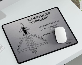 Puede incluir: Una ilustración en blanco y negro de un avión de combate Eurofighter Typhoon en una alfombrilla de ratón plateada. La alfombrilla de ratón incluye el texto "EUROFIGHTER "TYPHOON"" y las especificaciones técnicas del avión, incluida la velocidad máxima, el alcance y el techo.