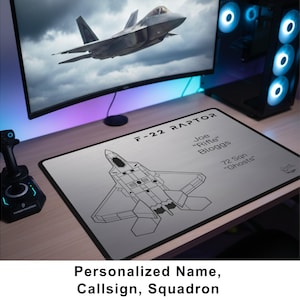 May include: A silver mousepad featuring a line drawing of an F-22 Raptor fighter jet. The text "F-22 RAPTOR" is at the top, with a name, callsign, and squadron details below. The bottom of the image reads "Personalized Name, Callsign, Squadron."