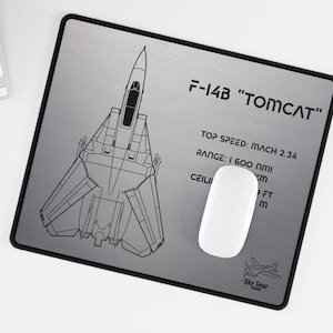 May include: A black and white line drawing of an F-14B Tomcat fighter jet on a silver mouse mat. The mouse mat includes the text "F-14B "TOMCAT"", "TOP SPEED: MACH 2.34", "RANGE: 1 600 NMI", "CEILI", "FT", "m", and "Sky Gear".