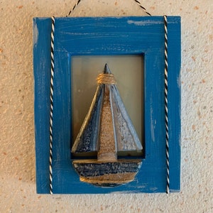 Könnte beinhalten: Ein blauer Holzrahmen mit einer weißen Seilschnur als Rahmen, der ein Holzsegelboot mit blau-weißem Segel und einem goldenen Seildetail enthält.