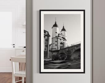 Pode incluir: Fotografia a preto e branco de um edifício histórico com duas torres e uma ponte em primeiro plano. O edifício tem uma fachada listrada e um telhado pontiagudo. A ponte é de pedra e tem um arco arredondado.