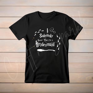 May include: Black t-shirt with white text that reads "I Solemnly Swear That I'm a Bridesmaid" with a graphic of a broom and footprints.