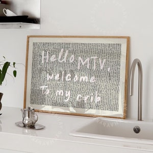 Może przedstawiać: Wydruk w ramie z tekstem "Hello MTV, welcome to my crib" w różowych literach na tle czarno-białego tekstu. Wydruk wisi na białej ścianie nad białym blatem z srebrnym czajnikiem i białą porcelanową umywalką.