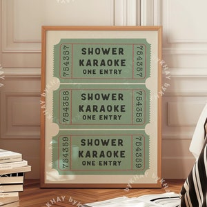May include: A framed print featuring three vintage-style tickets that read "Shower Karaoke One Entry". The tickets are green with red and white accents. The print is hanging on a white wall.