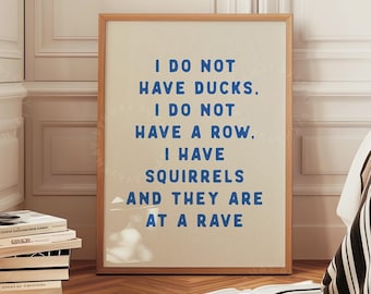 May include: A framed print with the text "I DO NOT HAVE DUCKS. I DO NOT HAVE A ROW. I HAVE SQUIRRELS AND THEY ARE AT A RAVE" in blue on a beige background. The print is in a room with a bed and a stack of books.