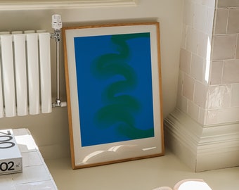 May include: A framed abstract print with a green and blue design. The print is hanging on a white wall in a room with a white radiator and a white tiled floor. A book and two paintbrushes are on the floor.