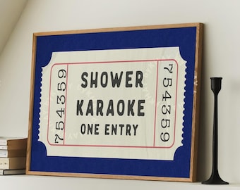 May include: A blue framed poster with a white ticket design. The ticket says "Shower Karaoke One Entry" in red and black text. The ticket number is 754359. Two black candle holders are on a white surface below the poster.