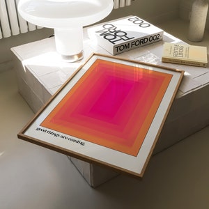 May include: A framed print featuring a geometric design in shades of orange, pink and red. The print has the text "good things are coming" at the bottom.
