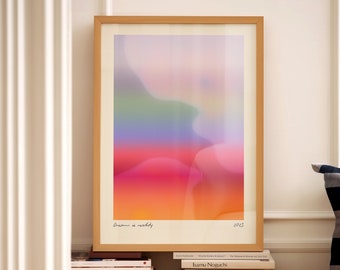 Pode incluir: Uma impressão de arte abstrata emoldurada com um degradê de cores que vai do rosa ao laranja, ao amarelo, ao azul e ao verde. A impressão é intitulada "Dream is reality" e é assinada "CRIS". A impressão está sobre uma pilha de livros.