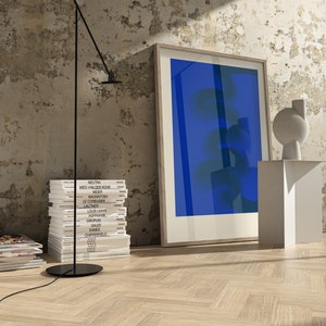 May include: A stack of books with the names of famous architects on the spines, a black floor lamp with a white shade, a white pedestal with a white abstract sculpture, and a framed blue abstract painting on a white wall.