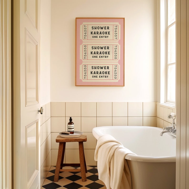 May include: A white bathroom with a white bathtub, a wooden stool, and a framed print of three pink tickets that say "Shower Karaoke One Entry".
