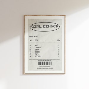 May include: A framed print featuring a receipt-style design with the text "GIRL DINNER" at the top. The receipt lists items like wine, crackers, salami, cheese, chips, and ice cream. The print has a beige background and a gold frame.