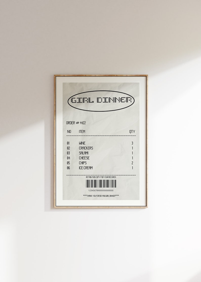 May include: A framed print featuring a receipt-style design with the text "GIRL DINNER" at the top. The receipt lists items like wine, crackers, salami, cheese, chips, and ice cream. The print has a beige background and a gold frame.