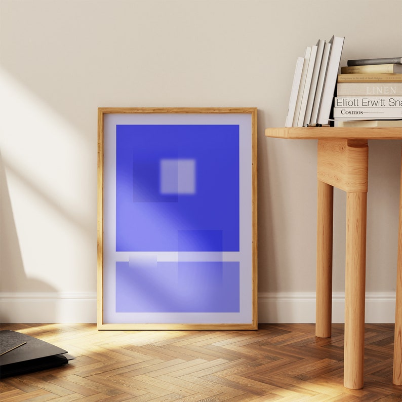 May include: A framed abstract print with a blue background and a white square in the center. The frame is made of natural wood and has a light brown finish.