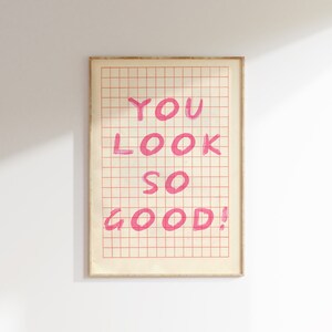 K&ouml;nnte beinhalten: Ein gerahmter Druck mit einem Gittermusterhintergrund. Die Worte "YOU LOOK SO GOOD!" sind in Pink auf dem Druck geschrieben.