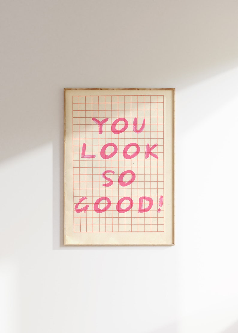 K&ouml;nnte beinhalten: Ein gerahmter Druck mit einem Gittermusterhintergrund. Die Worte "YOU LOOK SO GOOD!" sind in Pink auf dem Druck geschrieben.