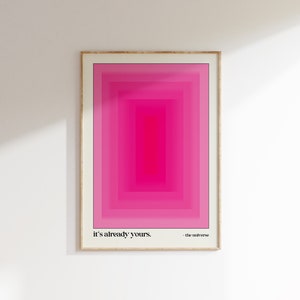 May include: A framed print with a pink and white geometric design. The text "it's already yours. - the universe" is at the bottom of the print.