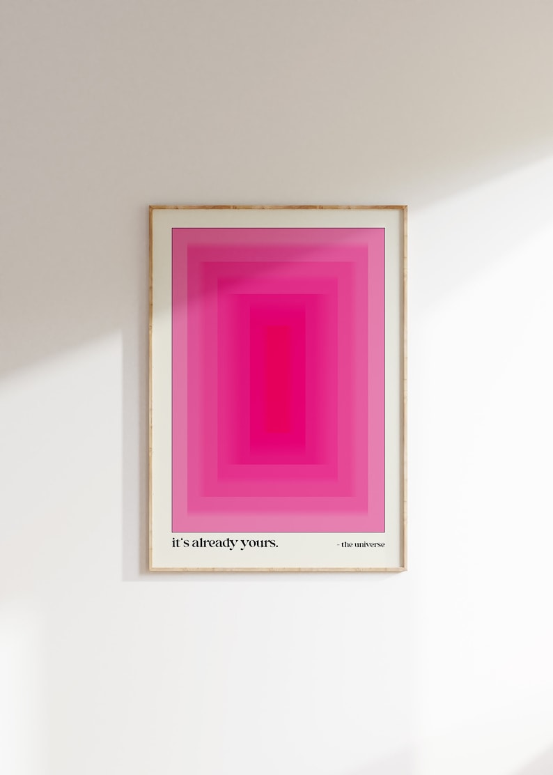 May include: A framed print with a pink and white geometric design. The text "it's already yours. - the universe" is at the bottom of the print.