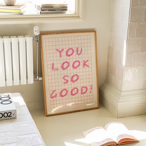 K&ouml;nnte beinhalten: Ein gerahmter Druck mit einem rosa Gittermuster und dem Text "YOU LOOK SO GOOD!" in rosa Schrift.