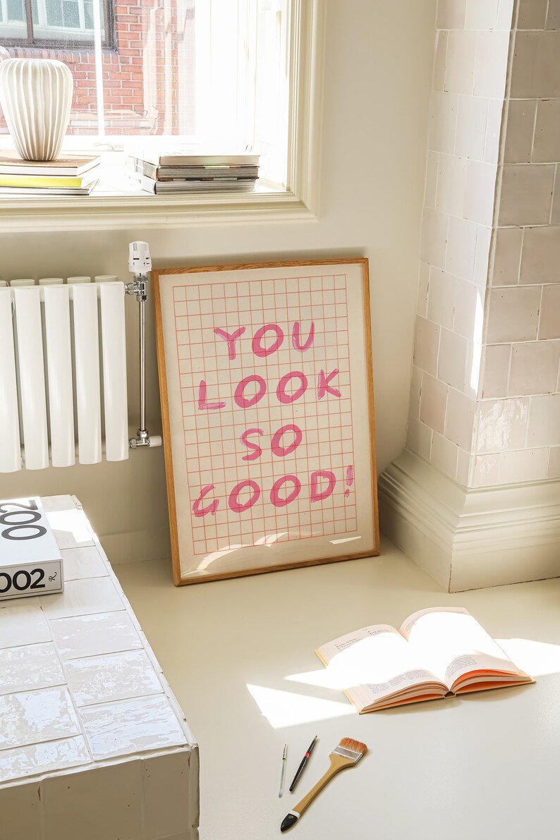 K&ouml;nnte beinhalten: Ein gerahmter Druck mit einem rosa Gittermuster und dem Text "YOU LOOK SO GOOD!" in rosa Schrift.