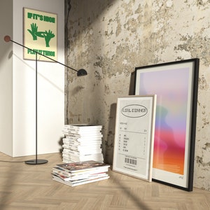 May include: An interior shot featuring framed art, magazines, and a modern floor lamp. One framed print has the text "IF IT'S NICE PLAY IT TWICE". Another print resembles a receipt with the text "GIRL DINNER". The floor lamp has a black stem and a round base.