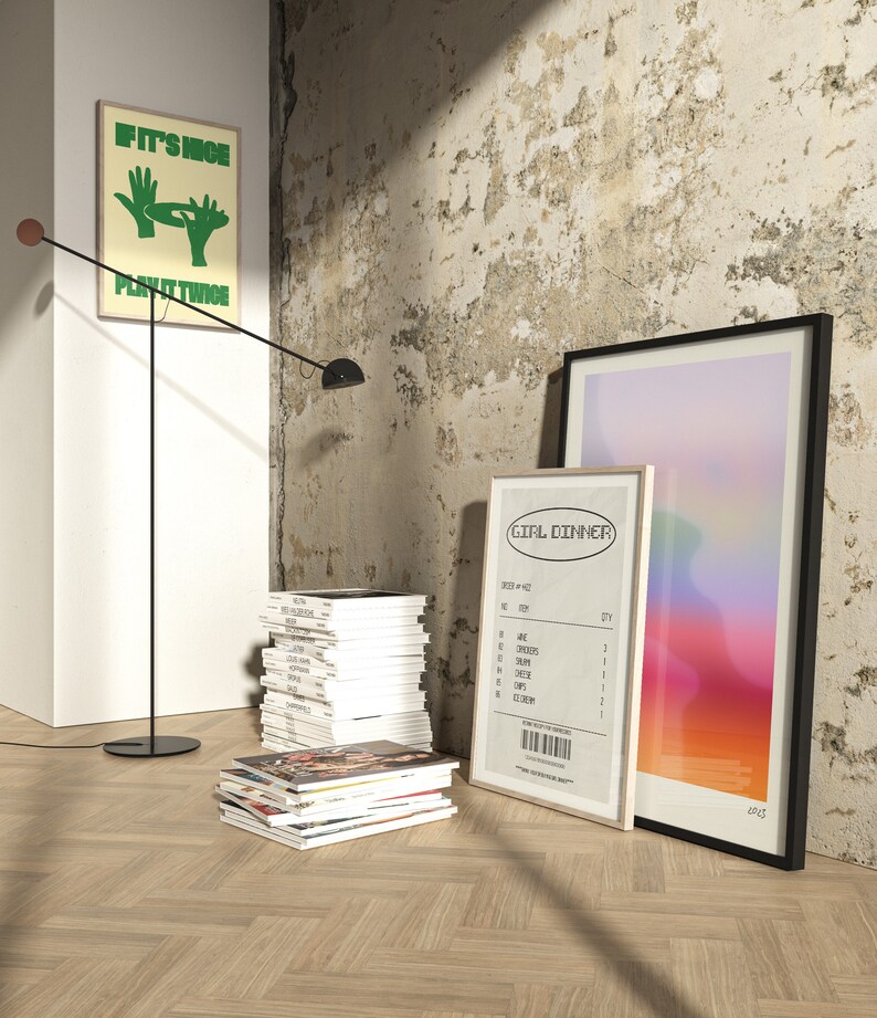 May include: An interior shot featuring framed art, magazines, and a modern floor lamp. One framed print has the text "IF IT'S NICE PLAY IT TWICE". Another print resembles a receipt with the text "GIRL DINNER". The floor lamp has a black stem and a round base.