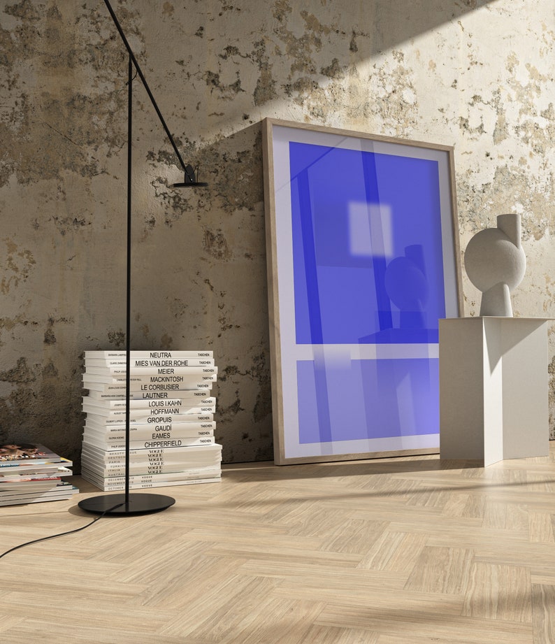 May include: A stack of books with the names of famous architects on the spines, a black floor lamp with a white ceiling, a white pedestal with a white abstract sculpture, and a framed blue poster on a white wall.
