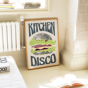 Pu&ograve; includere: Una stampa artistica incorniciata con un design retr&ograve;. L'opera presenta un hamburger stilizzato con una palla da discoteca come polpetta, lattuga e altri condimenti. Le parole "KITCHEN DISCO" sono scritte sopra e sotto l'hamburger in un font groovy.