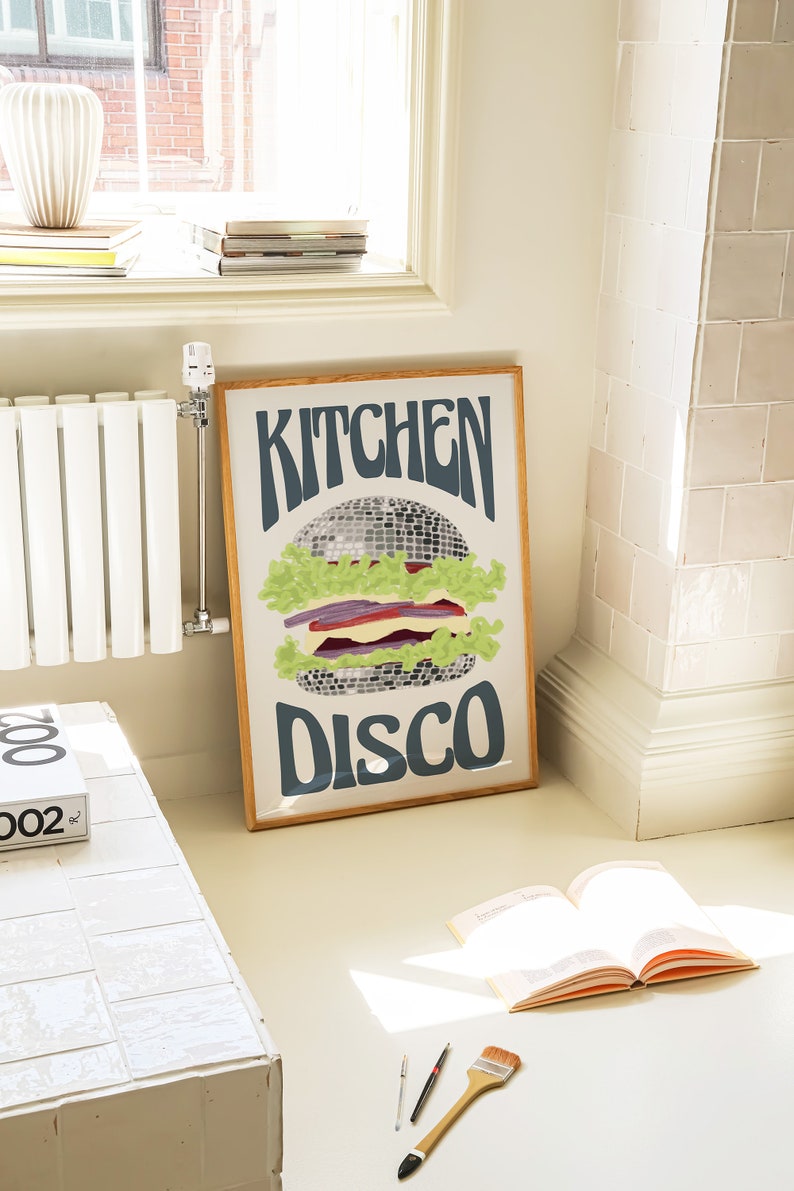 Pu&ograve; includere: Una stampa artistica incorniciata con un design retr&ograve;. L'opera presenta un hamburger stilizzato con una palla da discoteca come polpetta, lattuga e altri condimenti. Le parole "KITCHEN DISCO" sono scritte sopra e sotto l'hamburger in un font groovy.
