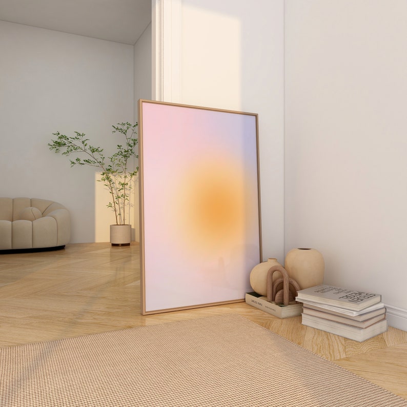 May include: A framed abstract art print with a gradient of pink, purple, and orange colors. The print is leaning against a white wall, with a stack of books and decorative vases in the foreground.