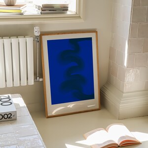 May include: A framed abstract print with a blue background and a dark blue, swirling, abstract design. The print is hanging on a white wall next to a white radiator.