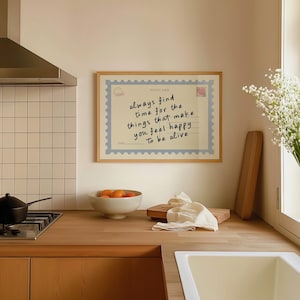 May include: A framed print with the text "always find time for the things that make you feel happy To be alive." The print is designed to look like a postcard with a light blue border and a postage stamp. The frame is made of light wood.