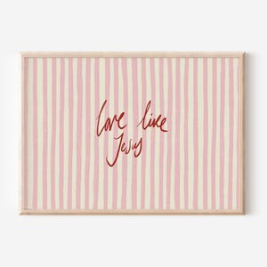 May include: Framed artwork with a light wood frame. The artwork features a pink and cream striped background with the words "love like Jesus" in red cursive script.