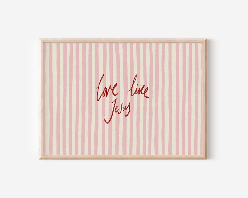 May include: Framed artwork with a light wood frame. The artwork features a pink and cream striped background with the words "love like Jesus" in red cursive script.