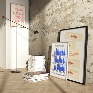 K&ouml;nnte beinhalten: Drei gerahmte Drucke an einer Wand mit einem Holzboden. Die Drucke sind alle wei&szlig; mit schwarzem Text und blauen Illustrationen. Der Text auf den Drucken lautet "You look so good!" "This kitchen is for drinking wine" und "Butter Get it while it's hot".