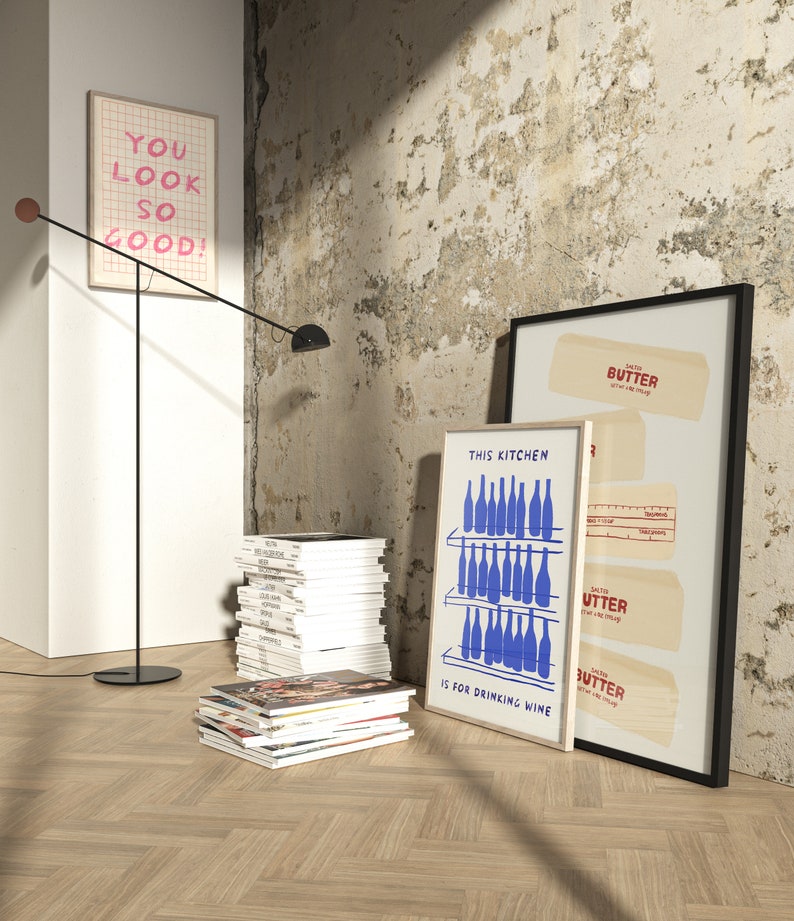 K&ouml;nnte beinhalten: Drei gerahmte Drucke an einer Wand mit einem Holzboden. Die Drucke sind alle wei&szlig; mit schwarzem Text und blauen Illustrationen. Der Text auf den Drucken lautet "You look so good!" "This kitchen is for drinking wine" und "Butter Get it while it's hot".