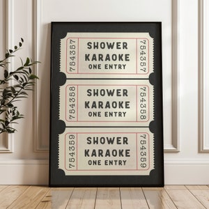 May include: Three vintage-style tickets with black text on a cream background. Each ticket reads "Shower Karaoke One Entry" with a ticket number at the top and bottom. The tickets are framed in a black frame against a white wall.