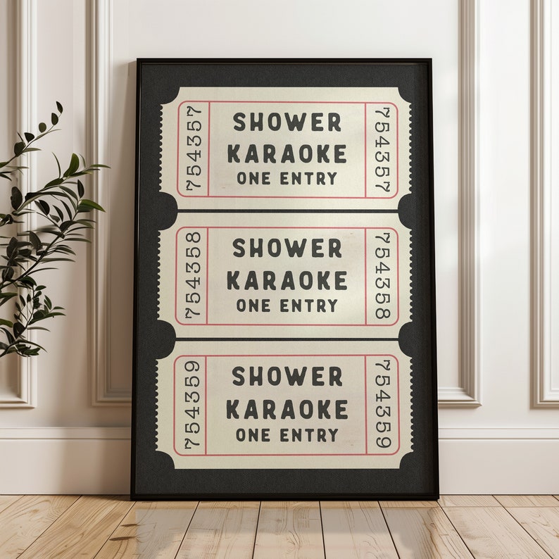 May include: Three vintage-style tickets with black text on a cream background. Each ticket reads "Shower Karaoke One Entry" with a ticket number at the top and bottom. The tickets are framed in a black frame against a white wall.