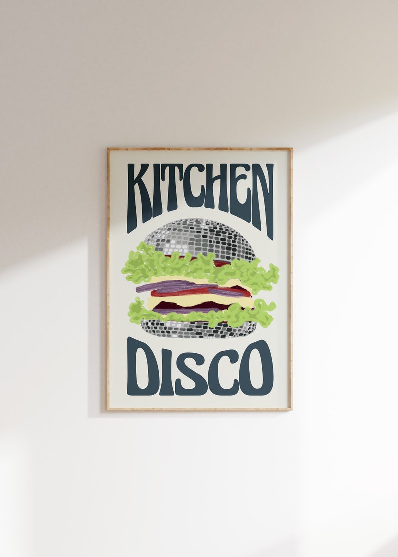 Pu&ograve; includere: Una stampa artistica incorniciata con un design di hamburger stravagante. L'hamburger &egrave; raffigurato con una palla da discoteca come polpetta, circondata da lattuga, pomodoro e altri condimenti. Le parole "KITCHEN DISCO" sono scritte sopra e sotto l'hamburger.